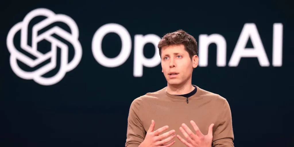 Sam Altman durante una presentación frente al logotipo de OpenAI mientras explica novedades relacionadas con la inteligencia artificial.