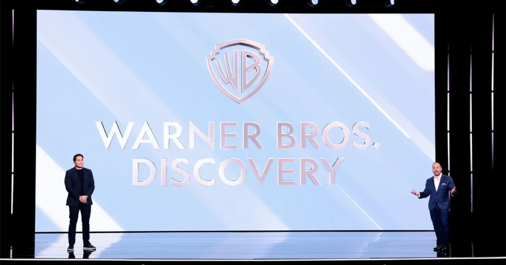 Ejecutivos de Warner Bros. Discovery sobre un escenario durante una presentación corporativa frente al logotipo de la compañía.
